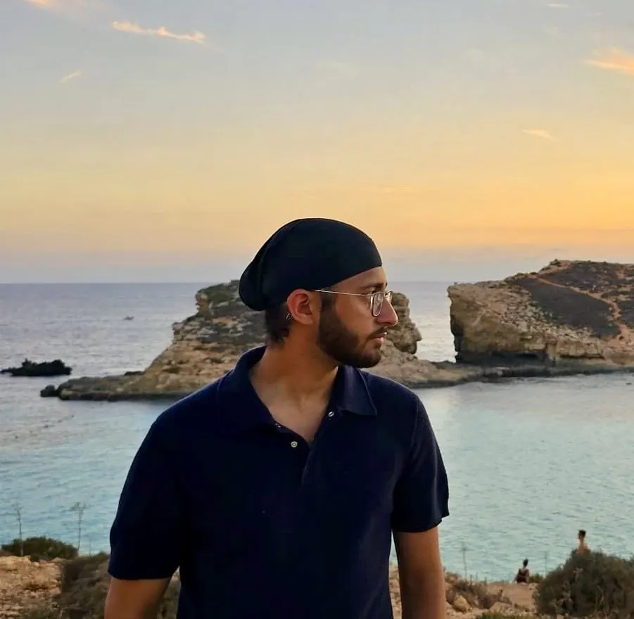 Anshjeet Singh in a navy polo shirt, looking to the side, with the sea behind him